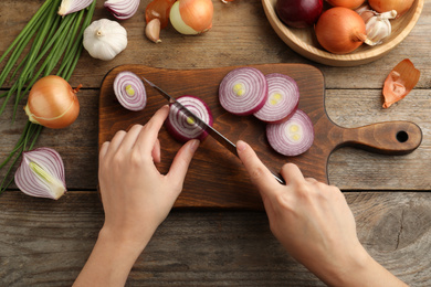 Photo of Woman cutting red onion on board at wooden table, top view