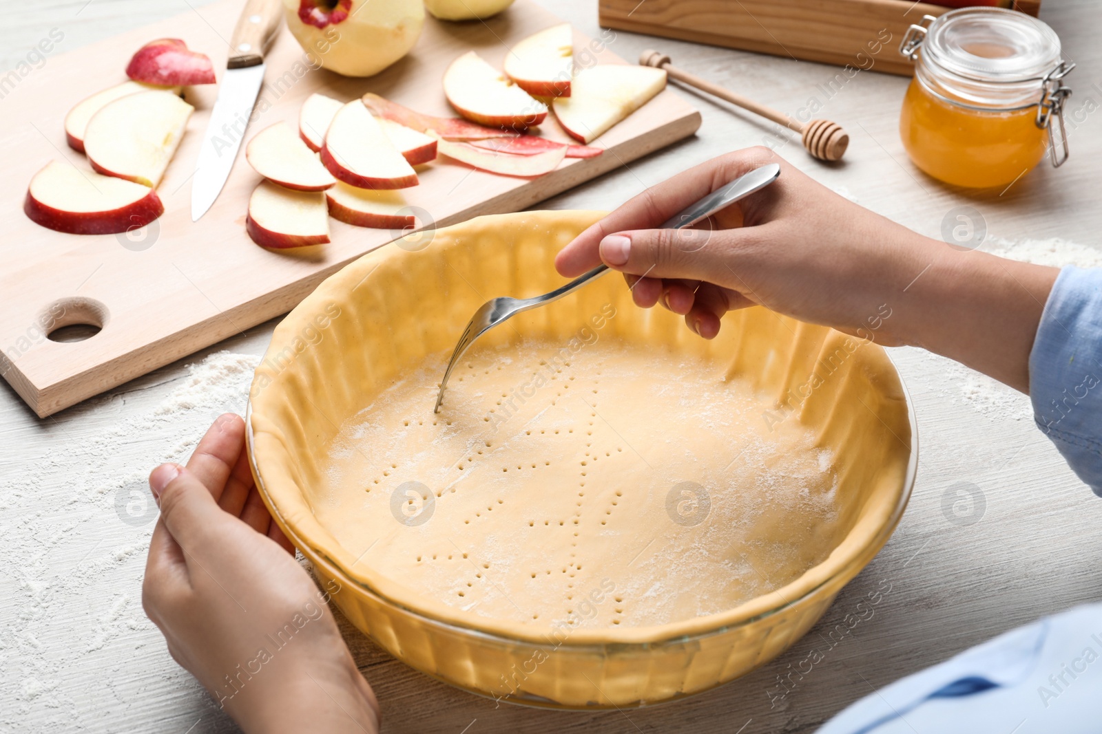 Photo of Woman making holes in raw dough with fork at white wooden table, closeup. Baking apple pie