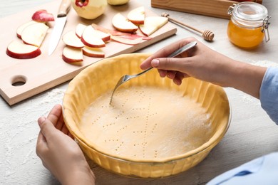 Photo of Woman making holes in raw dough with fork at white wooden table, closeup. Baking apple pie