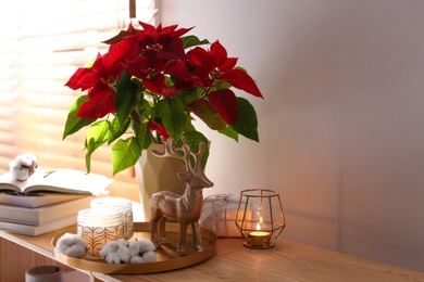 Beautiful poinsettia, burning candles and decorative deer on wooden rack indoors, space for text. Traditional Christmas flower