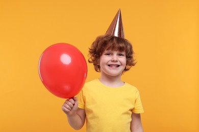 Happy little boy in party hat with balloon on orange background