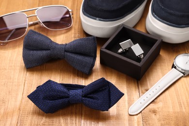 Photo of Stylish color bow ties, sunglasses, shoes, wristwatch and cufflinks on wooden background