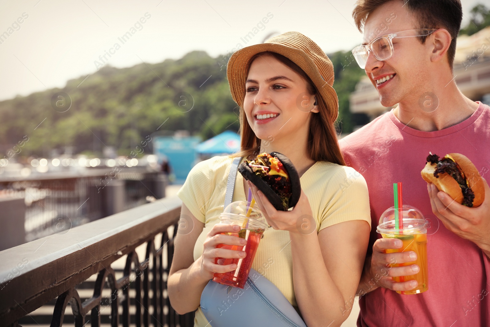 Photo of Young happy couple with burgers walking on city street. Space for text