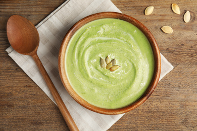 Photo of Delicious broccoli cream soup served on wooden table, flat lay