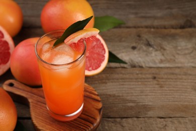 Photo of Tasty grapefruit drink with ice in glass and fresh fruits on wooden table. Space for text