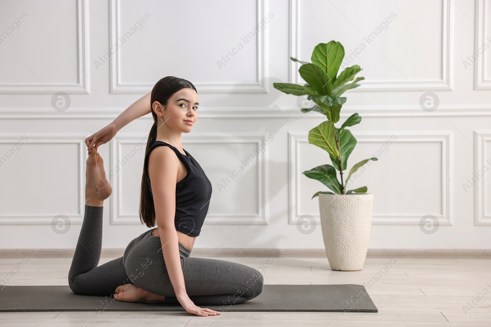 Photo of GIrl practicing one legged king pigeon asana on mat in yoga studio. Eka pada rajakapotasana pose