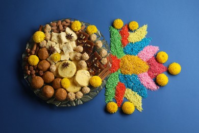 Photo of Diwali celebration. Tasty Indian sweets, colorful rangoli and chrysanthemum flowers on blue table, flat lay