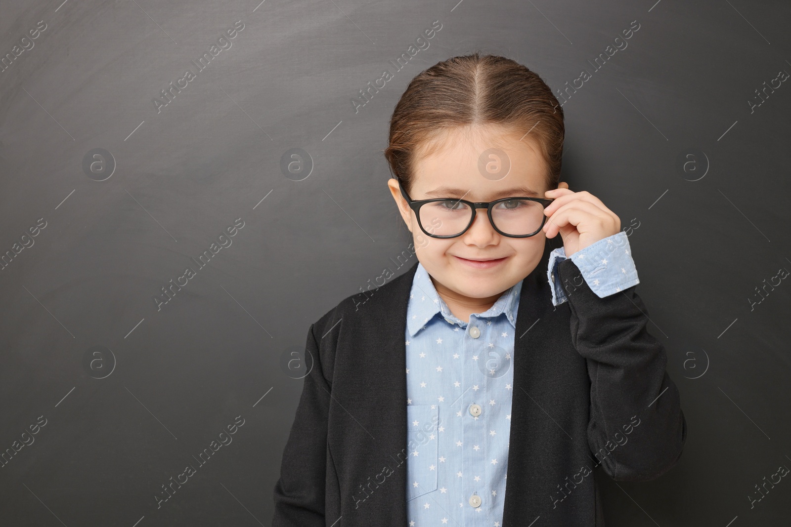 Photo of Happy little school child in uniform near chalkboard. Space for text