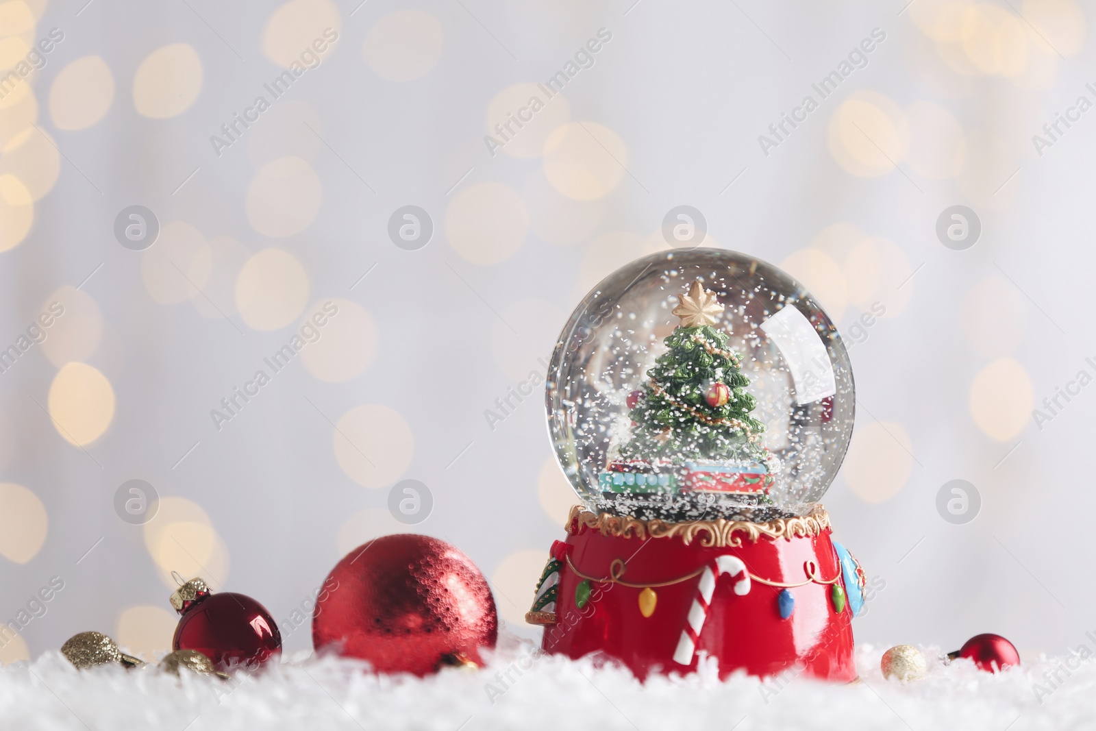 Photo of Beautiful snow globe and baubles against blurred Christmas lights. Space for text