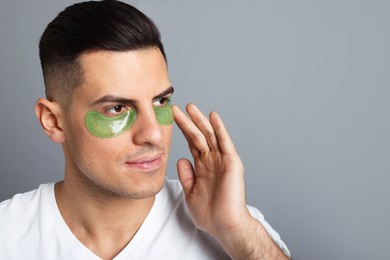 Photo of Man applying green under eye patch on grey background. Space for text