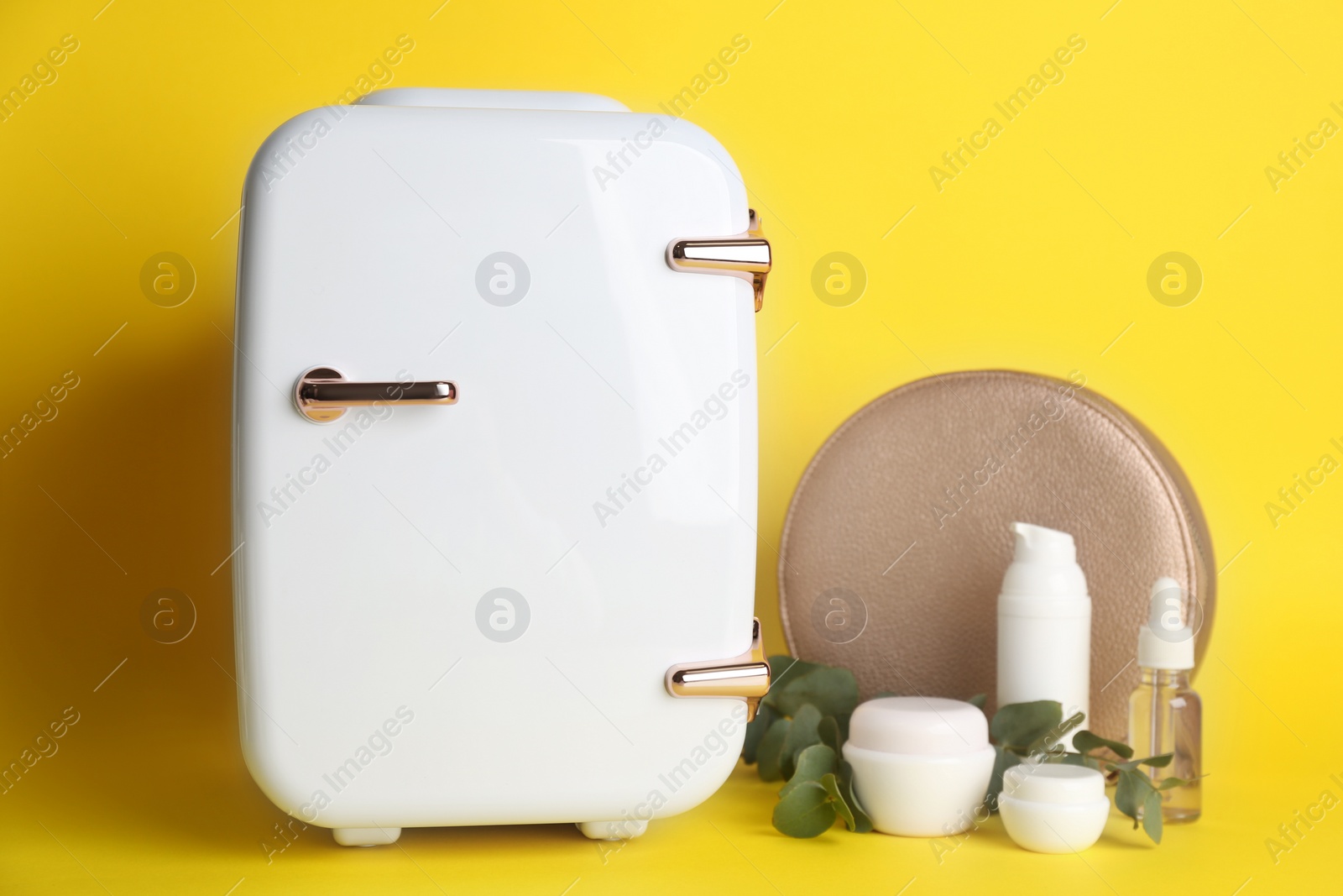 Photo of Cosmetic refrigerator and skin care products on yellow background