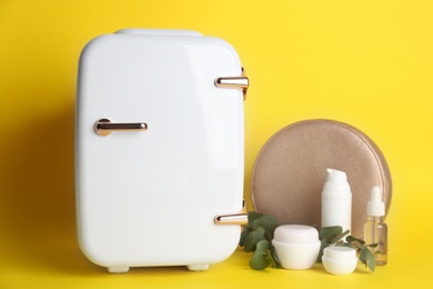 Cosmetic refrigerator and skin care products on yellow background