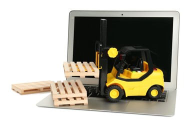 Laptop, toy forklift and wooden pallets on white background