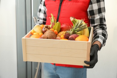 Photo of Courier holding crate with assortment of exotic fruits indoors, closeup