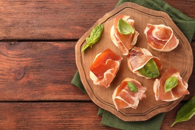 Photo of Board of tasty sandwiches with cured ham and basil leaves on wooden table, top view. Space for text