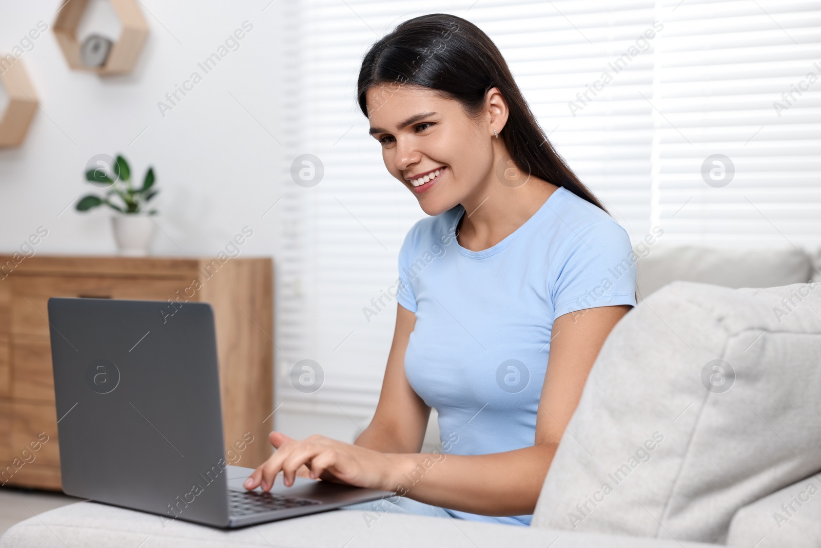 Photo of Happy young woman having video chat via laptop on sofa in living room