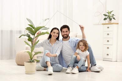 Photo of Family housing concept. Happy woman and her husband forming roof with their hands while sitting with daughter on floor at home