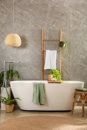 Photo of Modern white tub and beautiful green houseplants in bathroom. Interior design