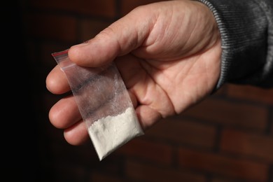 Photo of Drug addiction. Man with plastic bag of cocaine on blurred background, closeup