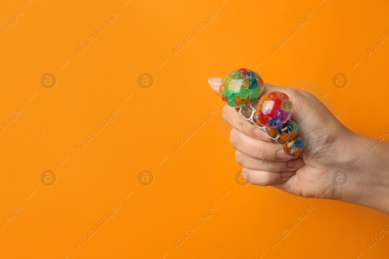 Photo of Woman squeezing colorful slime on orange background, closeup. Antistress toy