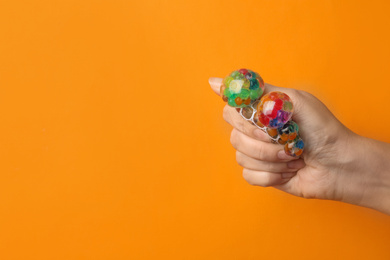 Photo of Woman squeezing colorful slime on orange background, closeup. Antistress toy