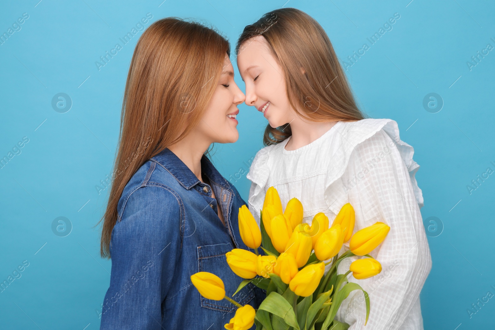 Photo of Mother and her cute daughter with bouquet of yellow tulips on light blue background