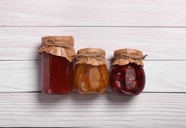 Photo of Jars with preserved fruit jams on white wooden table, flat lay