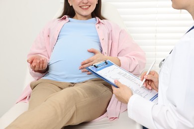 Photo of Doctor with results of laboratory test consulting smiling pregnant patient in clinic, closeup