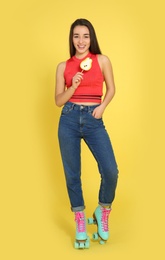 Full length portrait of young woman with lollipop and roller skates on color background