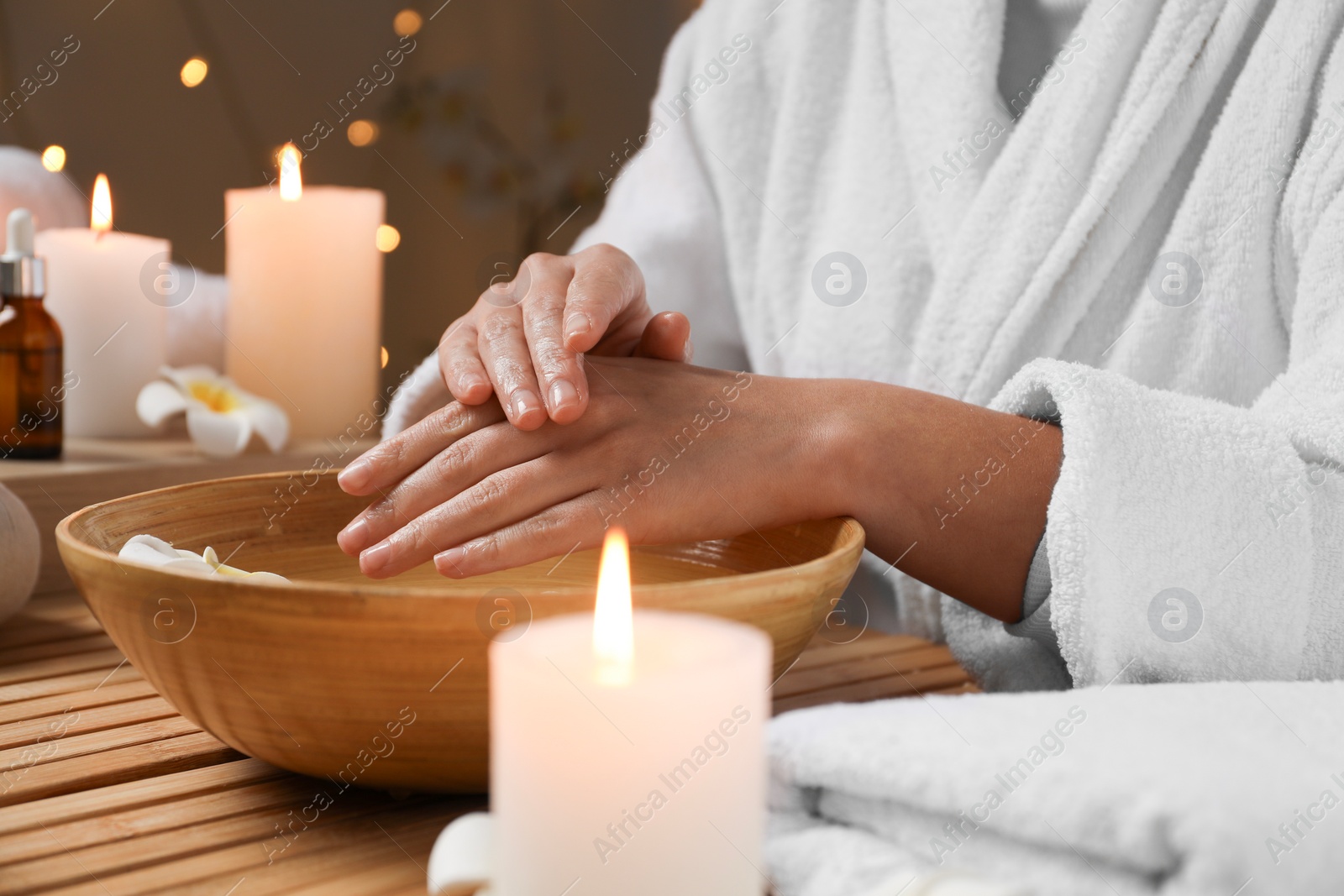 Photo of Woman soaking her hands in bowl of water at table, closeup. Spa treatment