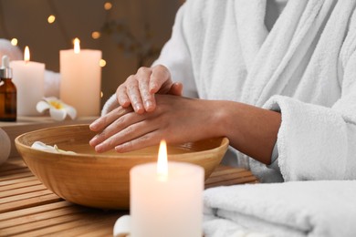 Photo of Woman soaking her hands in bowl of water at table, closeup. Spa treatment