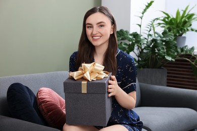 Beautiful young woman holding gift box on sofa in room