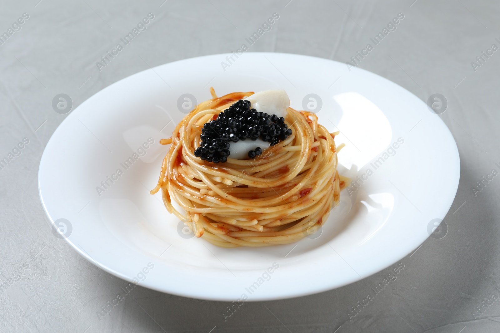 Photo of Tasty spaghetti with tomato sauce and black caviar on light grey table, closeup. Exquisite presentation of pasta dish