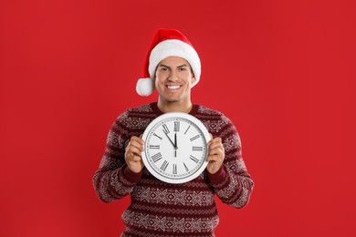 Photo of Man in Santa hat with clock on red background. New Year countdown