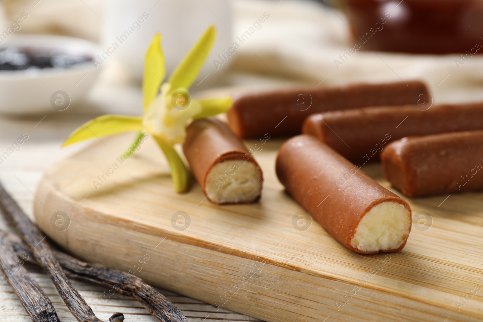 Photo of Glazed curd cheese bars, vanilla pods and flower on white wooden table, closeup