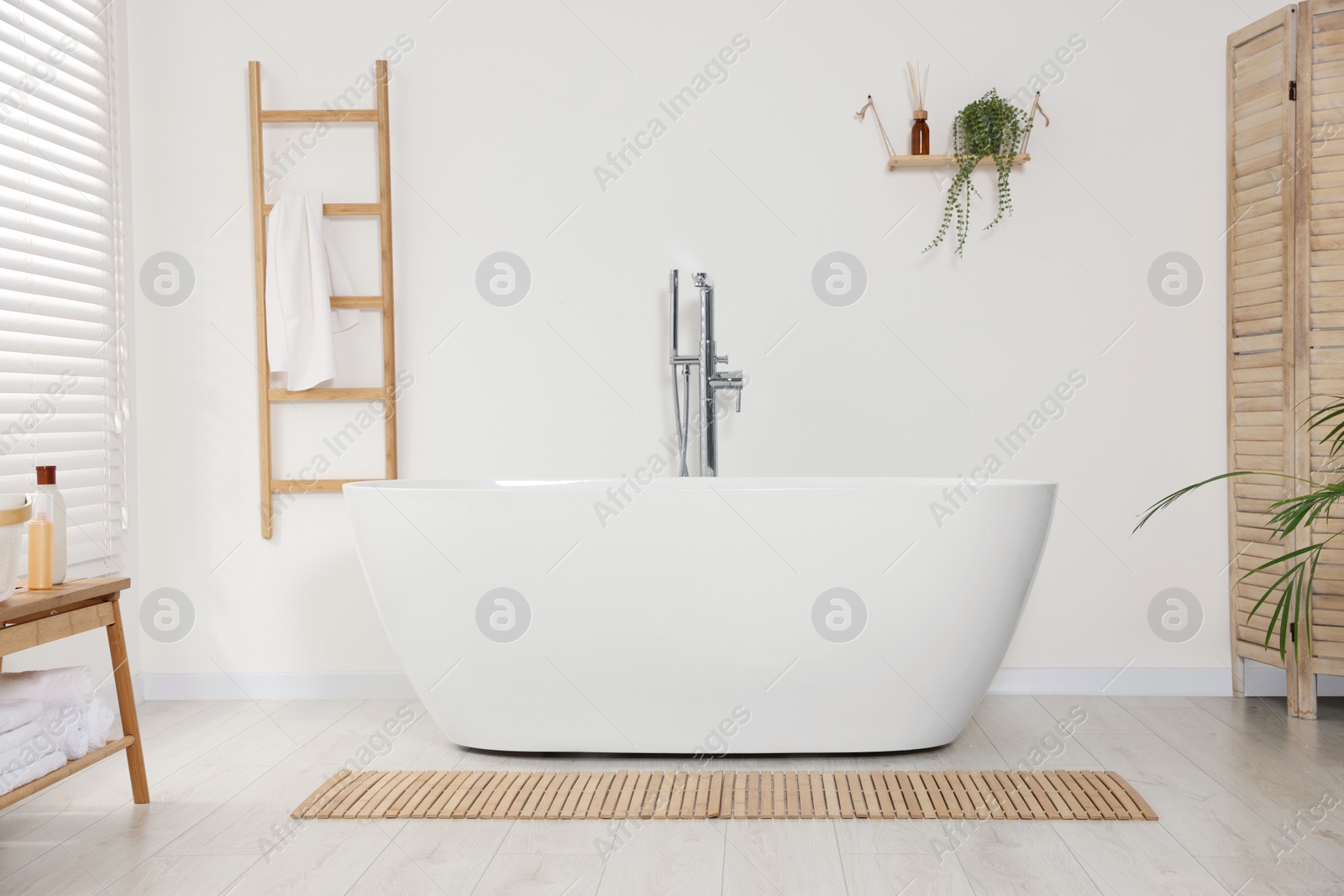 Photo of Stylish bathroom interior with ceramic tub and terry towel on wooden shelf