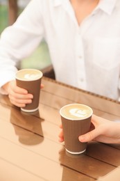 Photo of Women holding takeaway paper cups at table, closeup. Coffee to go