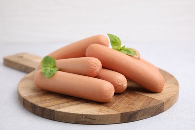 Photo of Delicious boiled sausages and basil on light gray table, closeup