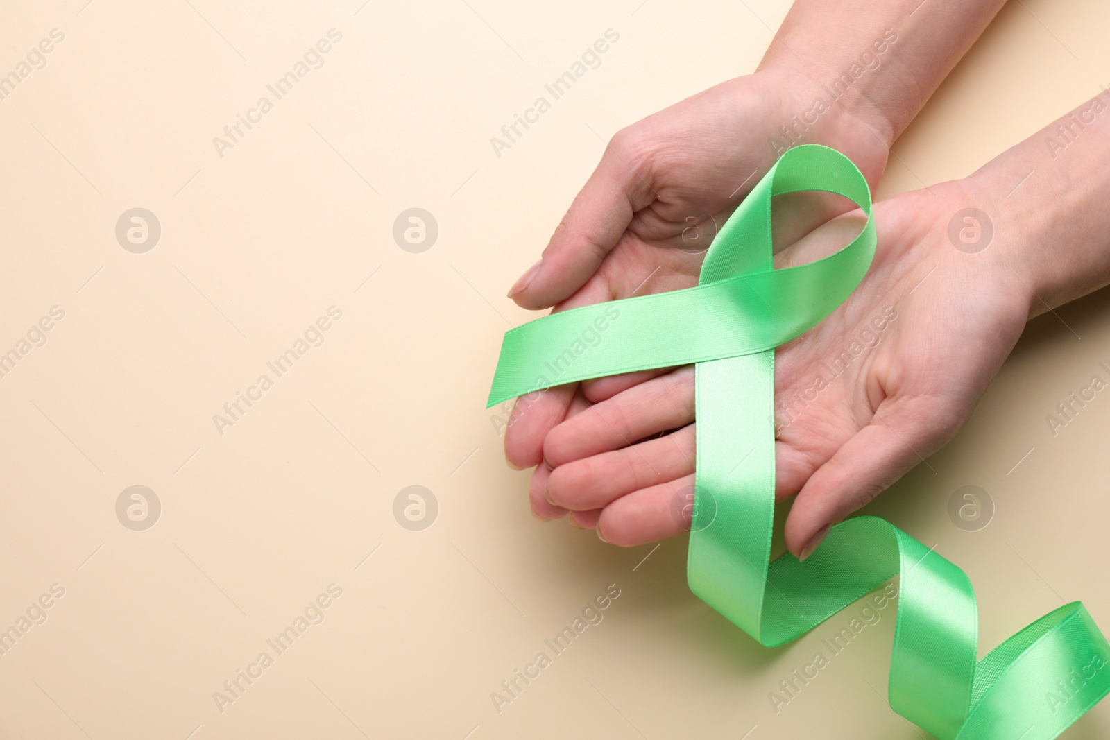 Photo of World Mental Health Day. Woman holding green ribbon on color background, closeup view with space for text