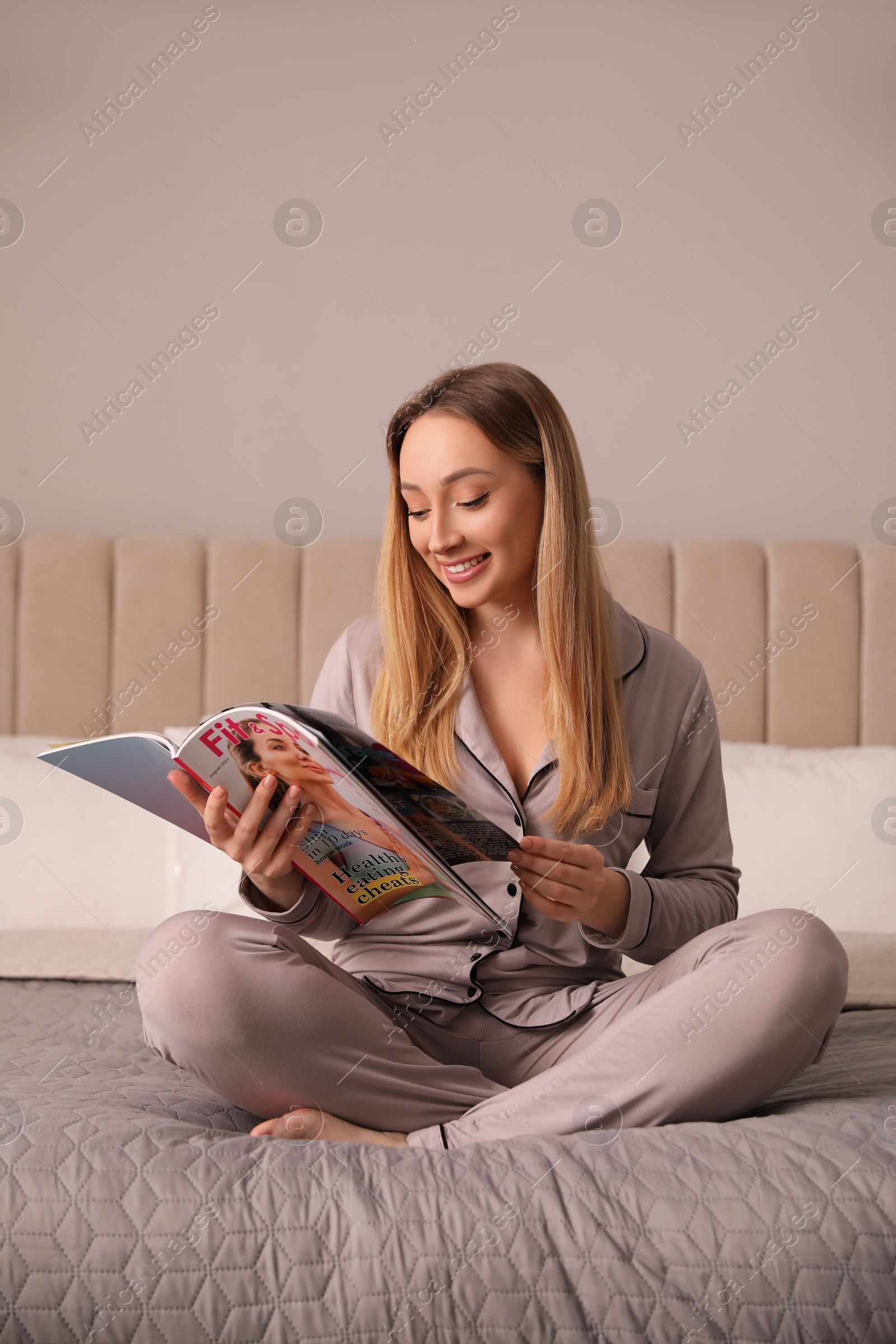 Photo of Happy woman reading magazine on bed indoors