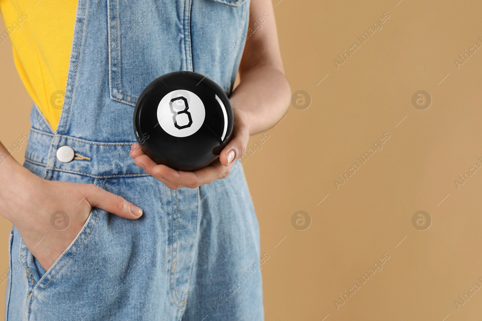 Photo of Woman holding magic eight ball on light brown background, closeup. Space for text