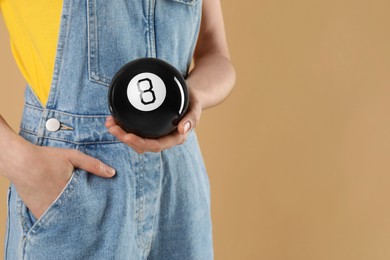 Woman holding magic eight ball on light brown background, closeup. Space for text