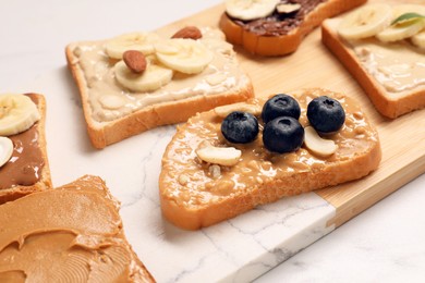 Photo of Toasts with different nut butters, fruits and nuts on white table, closeup