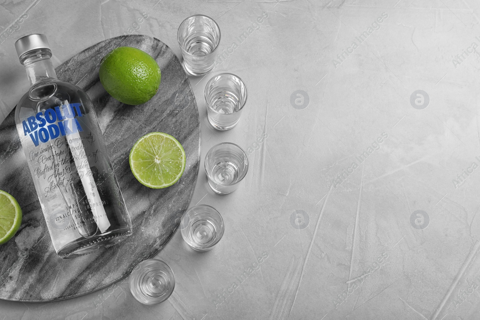 Photo of MYKOLAIV, UKRAINE - OCTOBER 04, 2019: Absolut vodka, limes and shot glasses on light grey table, flat lay. Space for text