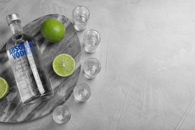 MYKOLAIV, UKRAINE - OCTOBER 04, 2019: Absolut vodka, limes and shot glasses on light grey table, flat lay. Space for text