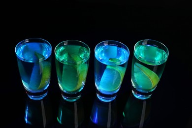 Alcohol drink with citrus wedges in shot glasses on mirror surface, above view