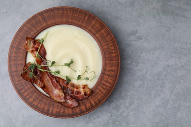 Photo of Delicious potato soup with bacon and microgreens in bowl on gray table, top view. Space for text