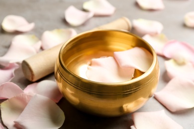 Photo of Golden singing bowl with petals on grey table, closeup. Sound healing