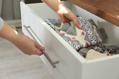 Photo of Woman taking warm knitted socks out of drawer indoors, closeup