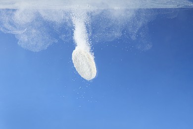 Photo of Effervescent pill dissolving in water on blue background, closeup